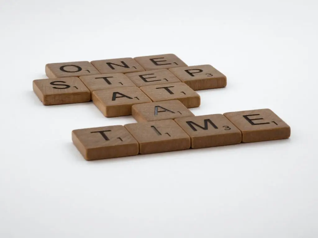 Scrabble tiles spell "ONE STEP AT A TIME" on a white background, embodying the approach embraced by Light Side Wellness Co in Portland therapy.